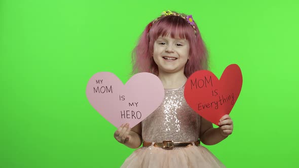 Child Girl Princess Holds Two Paper Hearts with Text About Mother. Mother's Day