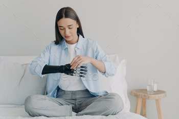 esis prosthesis parameters and functions. Bionic hand has processor chip and buttons. Attractive european girl adjusting her artificial arm at home.