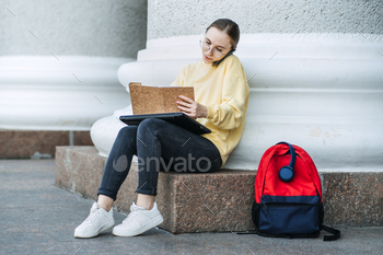 girl with laptop, papers and books near college