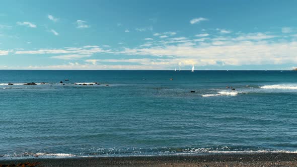 Unrecognized White Sailboats in the Turquoise Waters of the Ocean. Black Volcanic Sand Beach