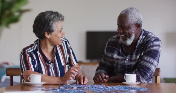 African american senior couple sitting by table doing puzzles drinking tea