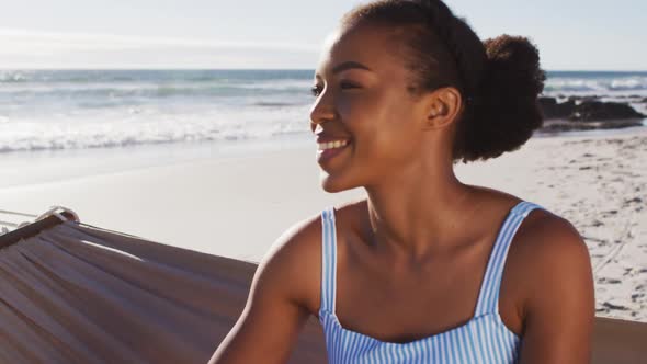 Close up of african american woman smiling while sitting on a hammock at the beach