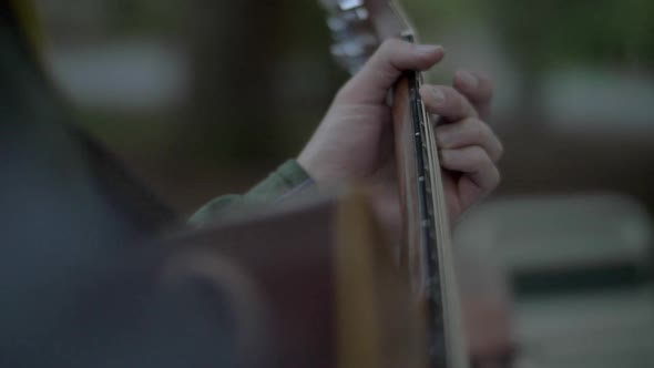 A Man Playing Guitar Outside at Dusk, Rotating Slow Motion Shot Focused on the Fingers Changing Chor