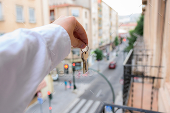 A man holds keys in a house with buildings in the background. Real state concept