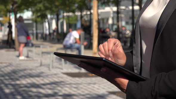 A Businesswoman Works on a Tablet in a Street in an Urban Area on a Sunny Day - Closeup