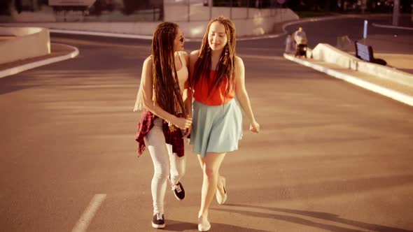 Two Happy Women with Dreads Walking on the Empty Road and Talking in Summer