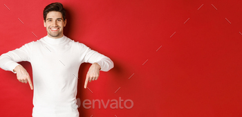 Image of smiling handsome man in white sweater inviting visit page, pointing fingers down and