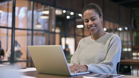 African Woman Smiling Toward Camera While Working on Laptop