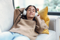 Beautiful woman listening to music with headphone while using smartphone lying on sofa at home. - PhotoDune Item for Sale