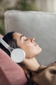 Beautiful woman listening to music with headphone while using smartphone lying on sofa at home. - PhotoDune Item for Sale