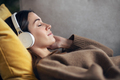 Beautiful woman listening to music with headphone while using smartphone lying on sofa at home. - PhotoDune Item for Sale