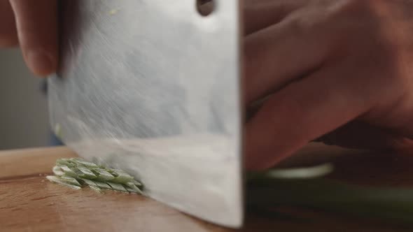 Front View of Young Chef Cutting Thin Slices of Green Onion with a Knife