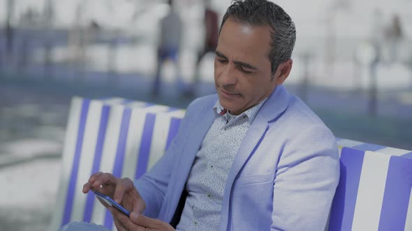 Smiling Hispanic Man Using Smartphone Outdoor