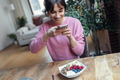 Beautiful young woman using her mobile phone while having healthy breakfast at home. - PhotoDune Item for Sale