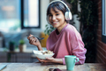 Beautiful young woman listening music with headphones while having healthy breakfast at home. - PhotoDune Item for Sale