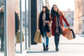 Two beautiful friends talking and having fun while walking on the city street with shopping bag. - PhotoDune Item for Sale