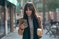 Pretty young woman using her mobile phone while drinking cup of coffee in street - PhotoDune Item for Sale