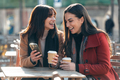 Two attractive friends enjoying coffee while looking smartphone and talking sitting on a terrace - PhotoDune Item for Sale