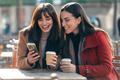 Two attractive friends enjoying coffee while looking smartphone and talking sitting on a terrace - PhotoDune Item for Sale
