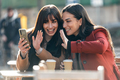 Two attractive friends enjoying coffee while doing a videocall with smartphone sitting on  terrace - PhotoDune Item for Sale