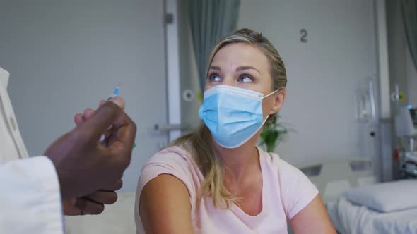 Caucasian female patient wearing face mask sitting in hospital bed waiting for injection