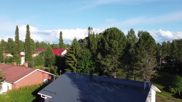 Aerial flyover rural small town with wooden apartment and forest trees during sunny day and blue sky