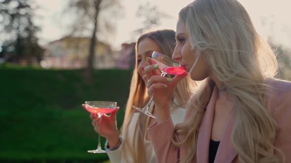 Two girlfriends drinking red champagne in park outdoors. Female persons having fun outside