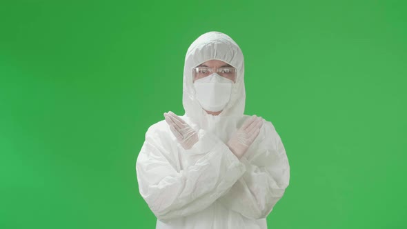 Asian Man Wear Protective Uniform PPE, Medical Face Mask And Show Stop Sign In Green Screen Studio