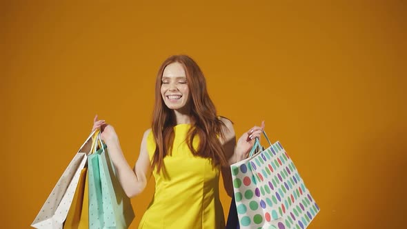 Smiling Beautiful Redhaired Woman in a Yellow Dress Enjoys Shopping Holding Several Colorful Paper
