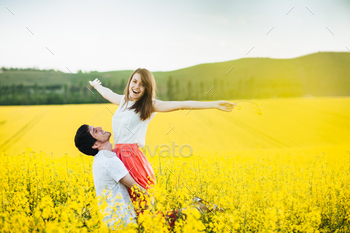 g on man`s hands, pose together on yellow flower field during sunny summer weather. Romantic couple have fun outdoor. Relationships concept.