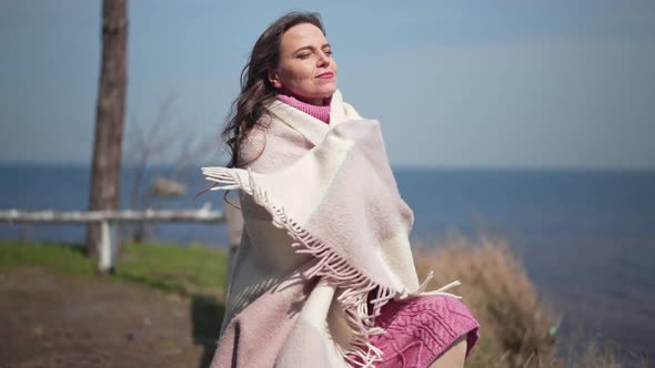 Portrait of Gorgeous Confident Caucasian Woman Smiling Wrapping in Blanket Sitting on River Bank