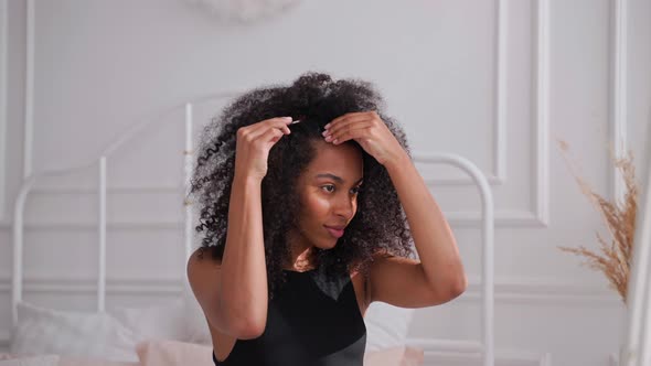 Black Woman Combing Her Afro Hair Sitting on a Bed and Looking in Mirror