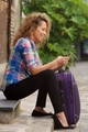 happy travel woman sitting on street with suitcase and looking at mobile phone - PhotoDune Item for Sale