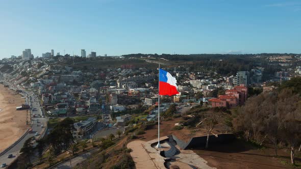 Aerial reverse view republic of Chile flag flying on Reñaca hilltop revealing downtown city coastal