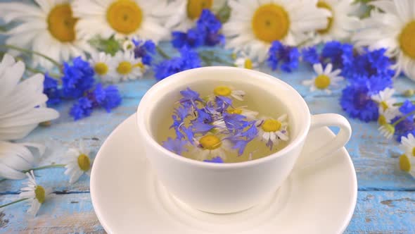 Brewing a tisanes from knapweeds and chamomile in white cup.