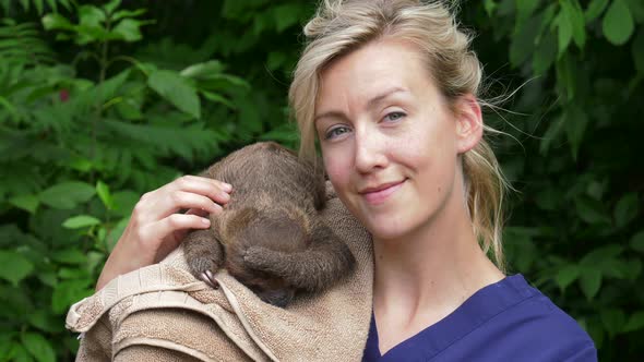 pretty veterinarian turns to camera and smiles petting baby sloth 4k