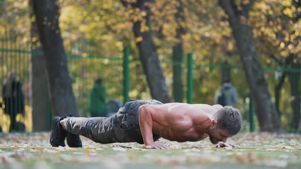 Muscular athlete doing push-ups outside.