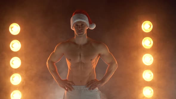 Portrait of Muscular Man Wearing Christmas Santa Hat Folded Hands on Smoky Background