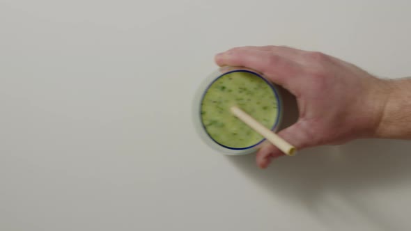Hand Puts Blue Transparent Glass with Green Detox Smoothie on White Table with Paper Ecofriendly