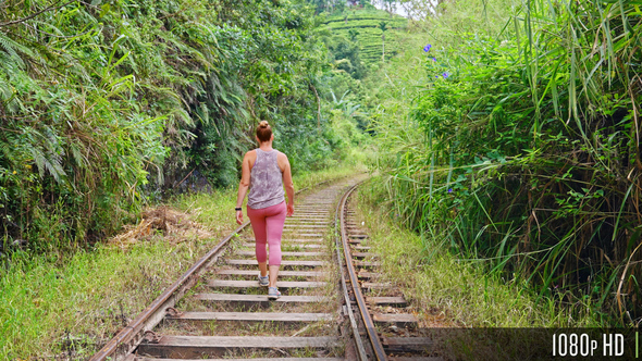 Parallax of Caucasian woman walking in slow motion down the middle of a train track in the jungle