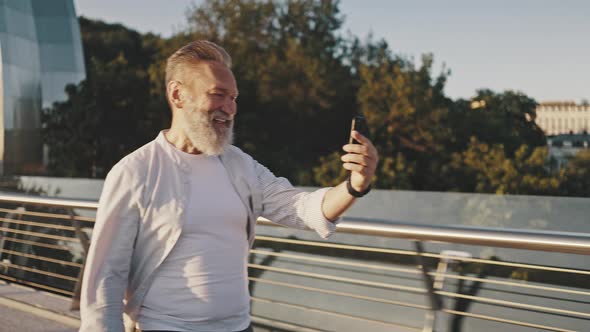 Bearded Senior Man Waves Hello to Wife on Phone Video Call