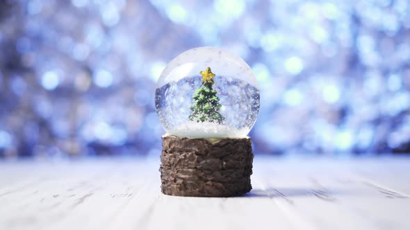 Closeup of Snowflakes Swirling Around a Christmas Tree Inside a Glass Ball