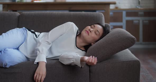 Exhausted or Bored Young Sleepy Asian Woman Falls Down on Sofa