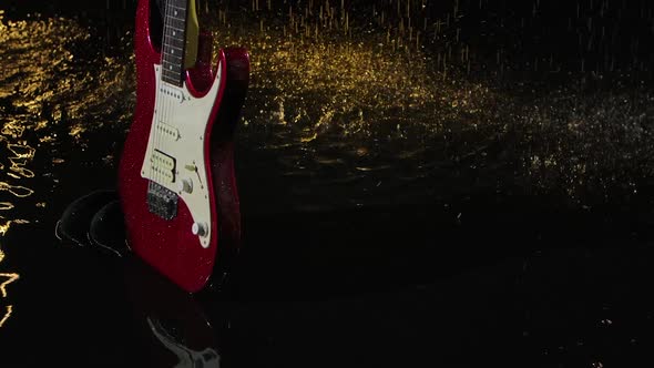 Wet Red Electric Guitar Falls on the Surface of the Water Illuminated By Yellow Light