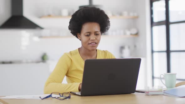 Happy african american woman sitting at table using laptop