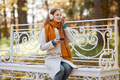 A young red-haired woman is sitting on a bench in an autumn park - PhotoDune Item for Sale