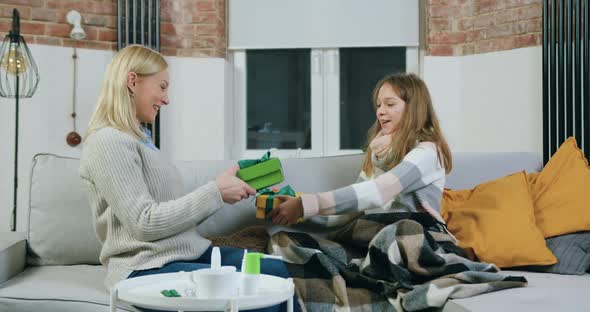 Mom and Daughter Which Sitting in Living-Room and Exchanging Gifts with Each Other, then Hugging