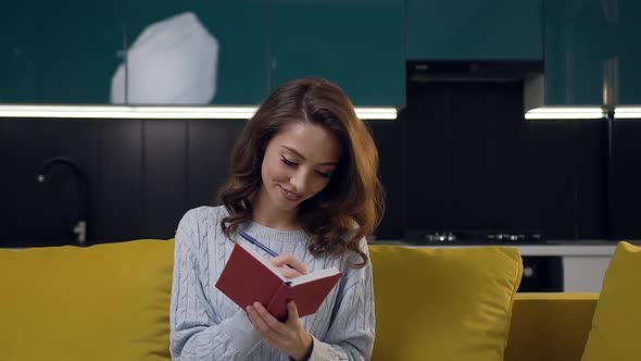 Charming Dreamy Lady with Wavy Hair Sitting on the Kitchen Sofa