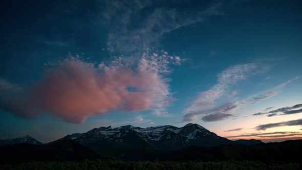 Time lapse of clouds lighting up at sunset over snow capped mountain