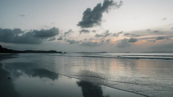 Timelapse of waves swashing on long beach in Asia at dusk creating reflections of sky in sand